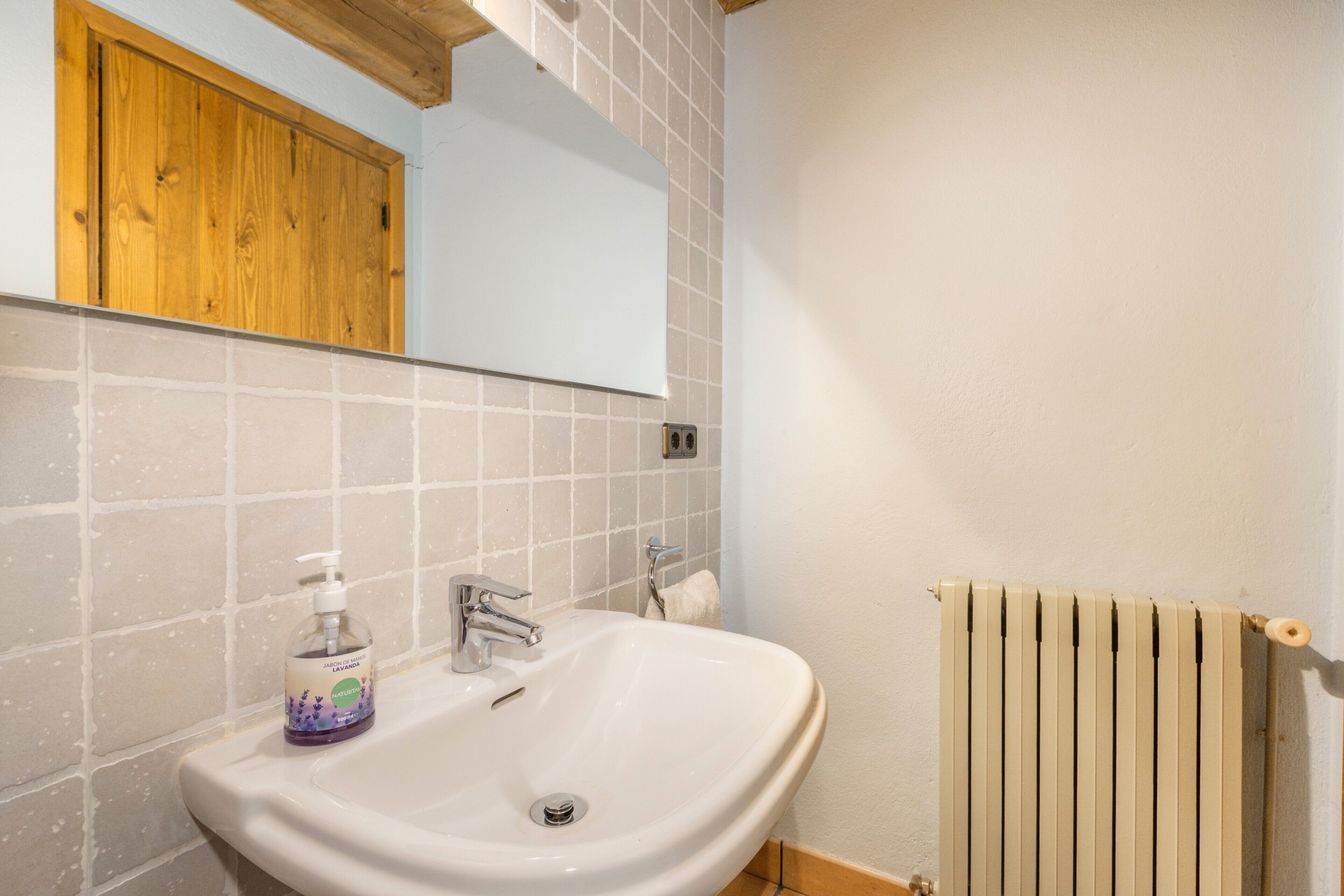 Un baño con lavamanos blanco, un espejo, un armario de madera y un radiador.