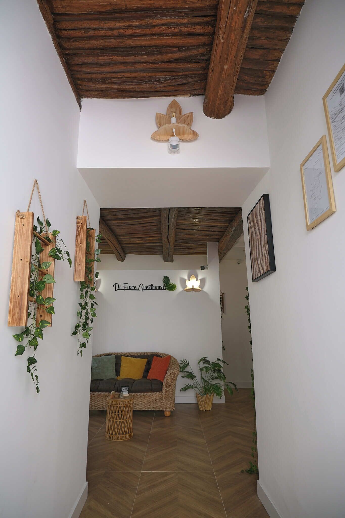 A cozy interior with a wooden ceiling, a wicker sofa, and a wall-mounted sign reading "Di Fiore Guesthouse".