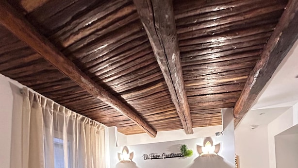 A cozy room with a wicker sofa, a small round table, and a ceiling with exposed beams. - Di Fiore Guesthouse (Naples)