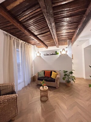 Ein gemütliches Zimmer mit einem Korbssofa, einem kleinen runden Tisch und einer Decke mit freiliegenden Balken.