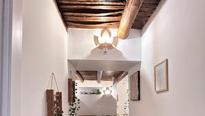A hallway with a herringbone floor, white walls, and a wooden ceiling. There is a sofa with cushions and a small table with a plant. - Di Fiore Guesthouse (Naples)