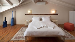 A bedroom with a sloped ceiling, a bed with white linens, two bedside lamps, a red ottoman, and a wooden headboard. - Dimore Holiday Home Silva (Rovinj)