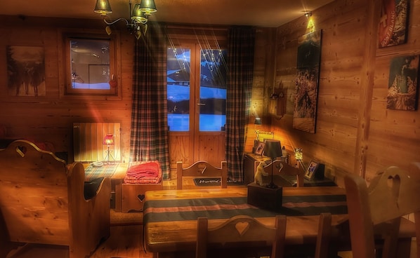 A cozy cabin interior with a wooden interior, a bed with a plaid blanket, a table with chairs, and a window with curtains. - Cozy room in the center of Megève (Megève)