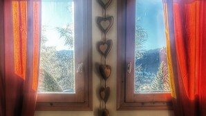 Une chambre à coucher avec une tête de lit en bois, deux fenêtres avec des rideaux et une vue sur les arbres à l’extérieur.