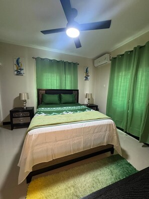A bedroom with a bed, two bedside tables, a ceiling fan, green curtains, and wall art. - Jahiem's Paradise (Ocho Rios)