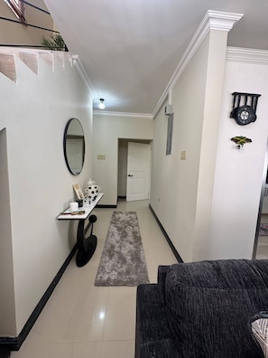 A hallway with a white door, a small table with a mirror, and a clock on the wall. - Jahiem's Paradise (Ocho Rios)