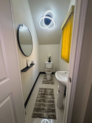 A bathroom with a toilet, sink, mirror, and a decorative light fixture. - Jahiem's Paradise (Ocho Rios)