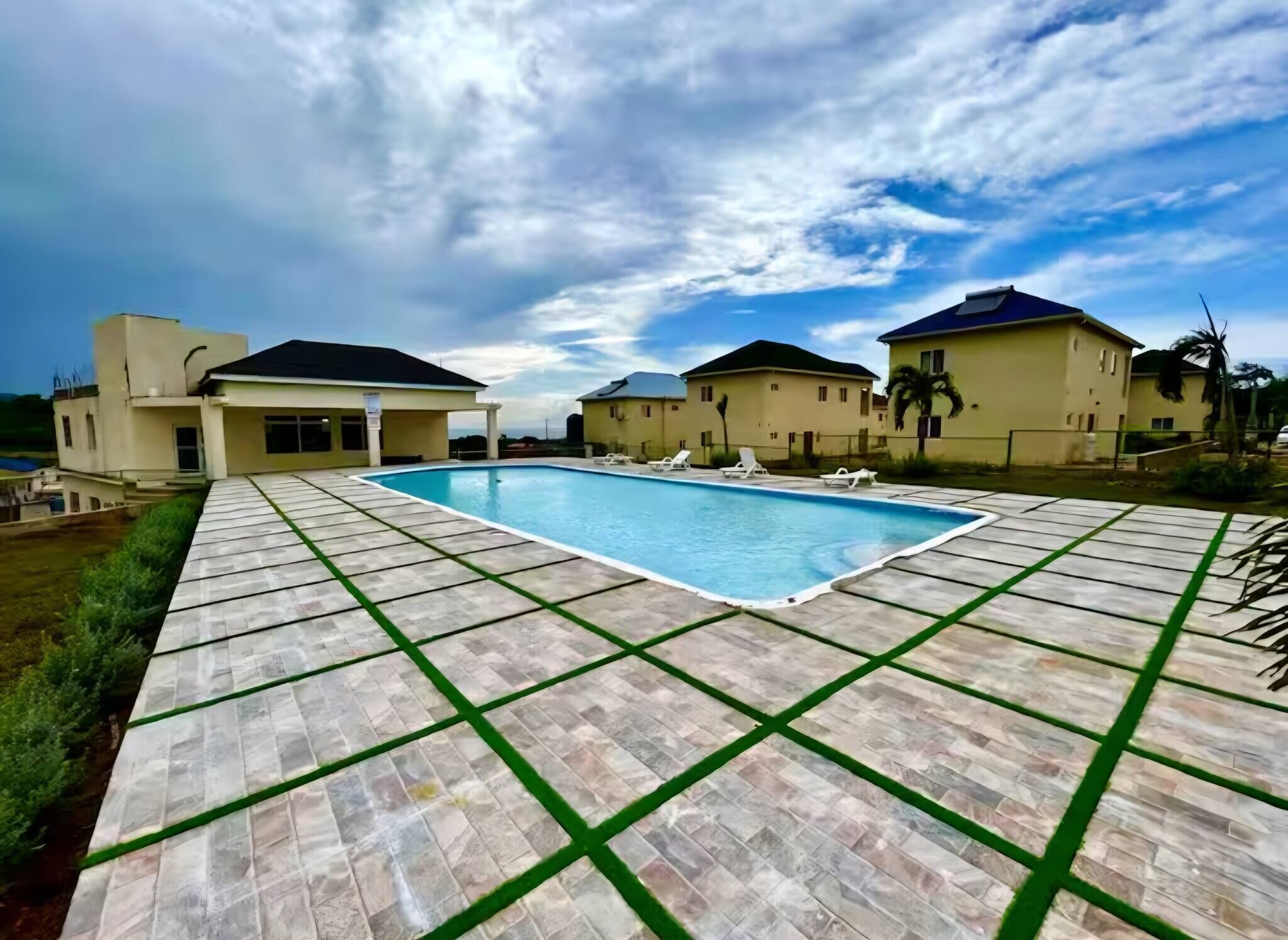 Une piscine avec une terrasse carrelée, entourée de maisons aux toits plats, sous un ciel dégagé.