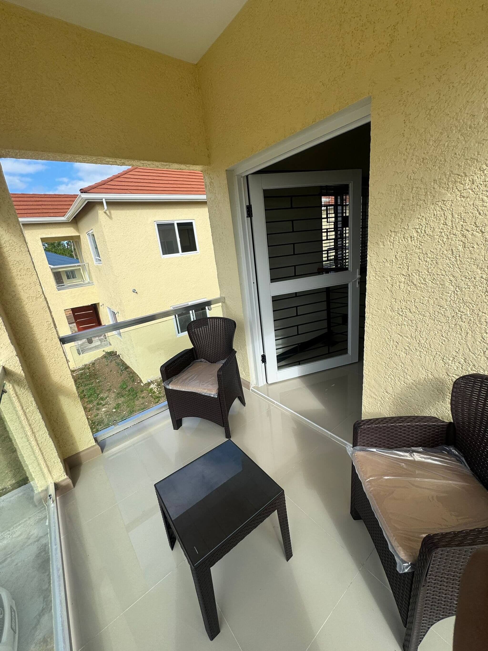 A balcony with wicker furniture, a sliding glass door, and a view of neighboring buildings.