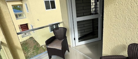 A balcony with wicker furniture, a sliding glass door, and a view of neighboring buildings.