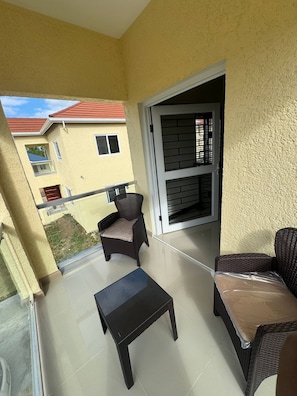 A balcony with wicker furniture, a sliding glass door, and a view of neighboring buildings. - Jahiem's Paradise (Ocho Rios)
