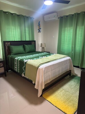 Ein Schlafzimmer mit einem Bett, einem Nachttisch, einer Lampe und einem grünen Vorhang.