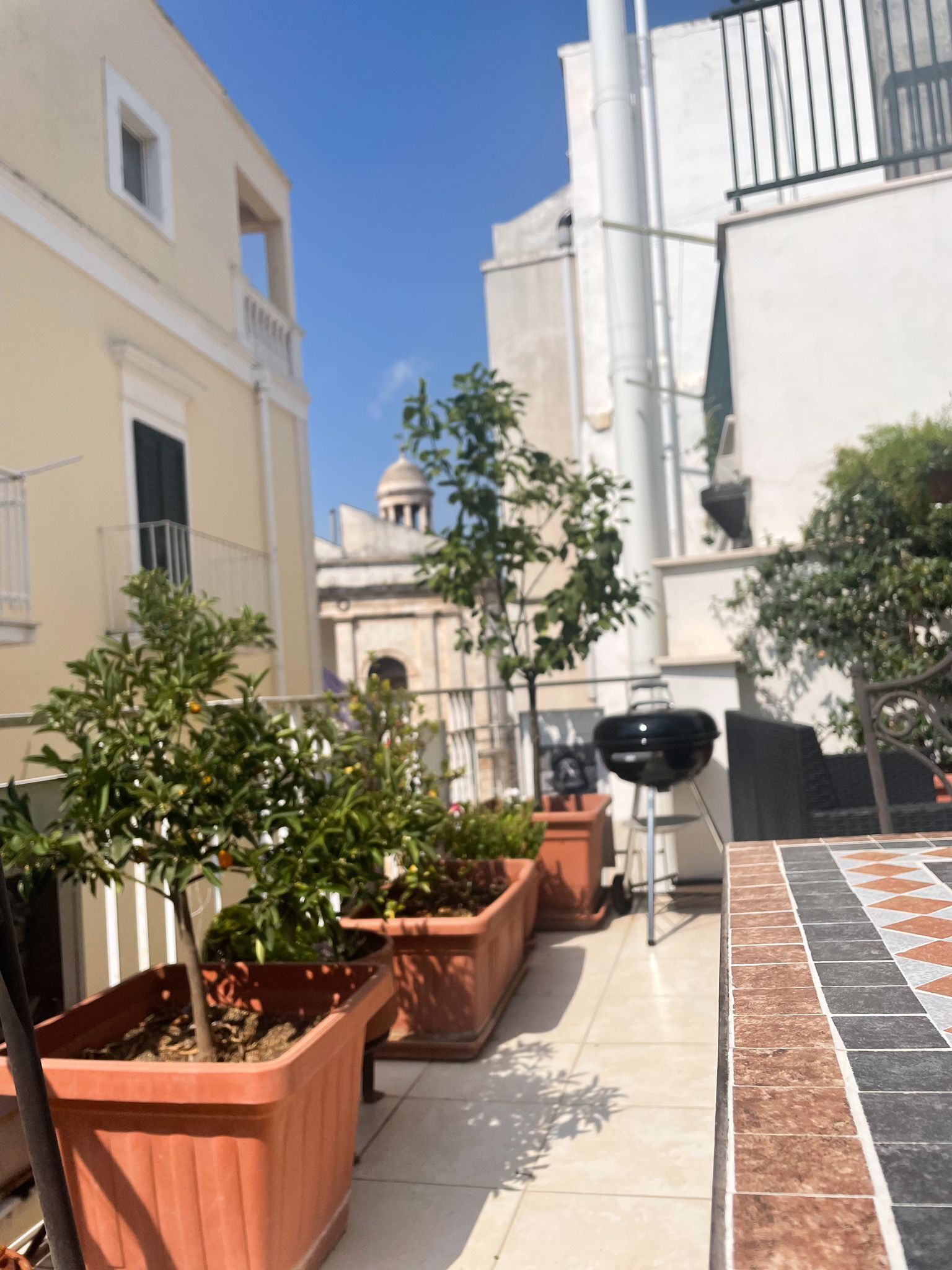 A courtyard with potted plants, a barbecue grill, and tiled flooring.