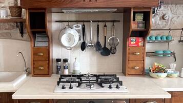Una cocina con pared de piedra, un mueble de madera con cajones, una estufa a gas y utensilios colgantes.