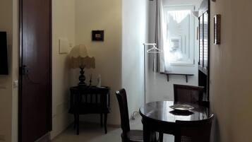 Un pasillo con una televisión montada en la pared, una puerta, una mesita con una lámpara y un comedor con sillas y una mesa.