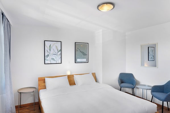 Habitación de hotel con una cama, dos sillas, una mesita y dos cuadros en la pared.