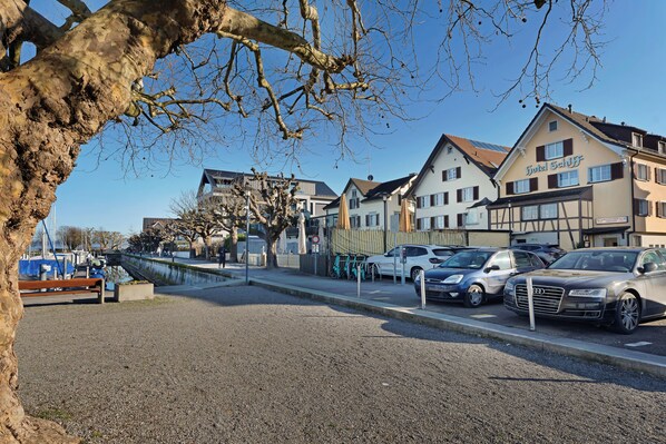 A hotel with a traditional European facade, a parking area with cars, and a tree in the foreground. - Hotel Schiff - Self Check-in (Horn)