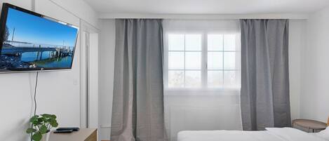 Una habitación de hotel moderna con una cama grande, un televisor montado en la pared, un escritorio con una planta y una ventana con cortinas.
