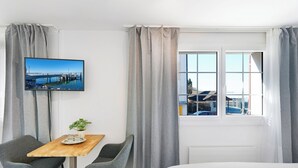 A hotel room with a bed, a TV mounted on the wall, a dining table with two chairs, and a window with curtains.