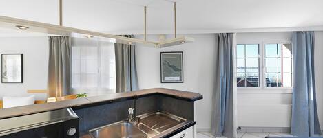 A modern kitchen with a Bosch microwave, stainless steel sink, and a black countertop. There is a window with curtains and a view of the city.