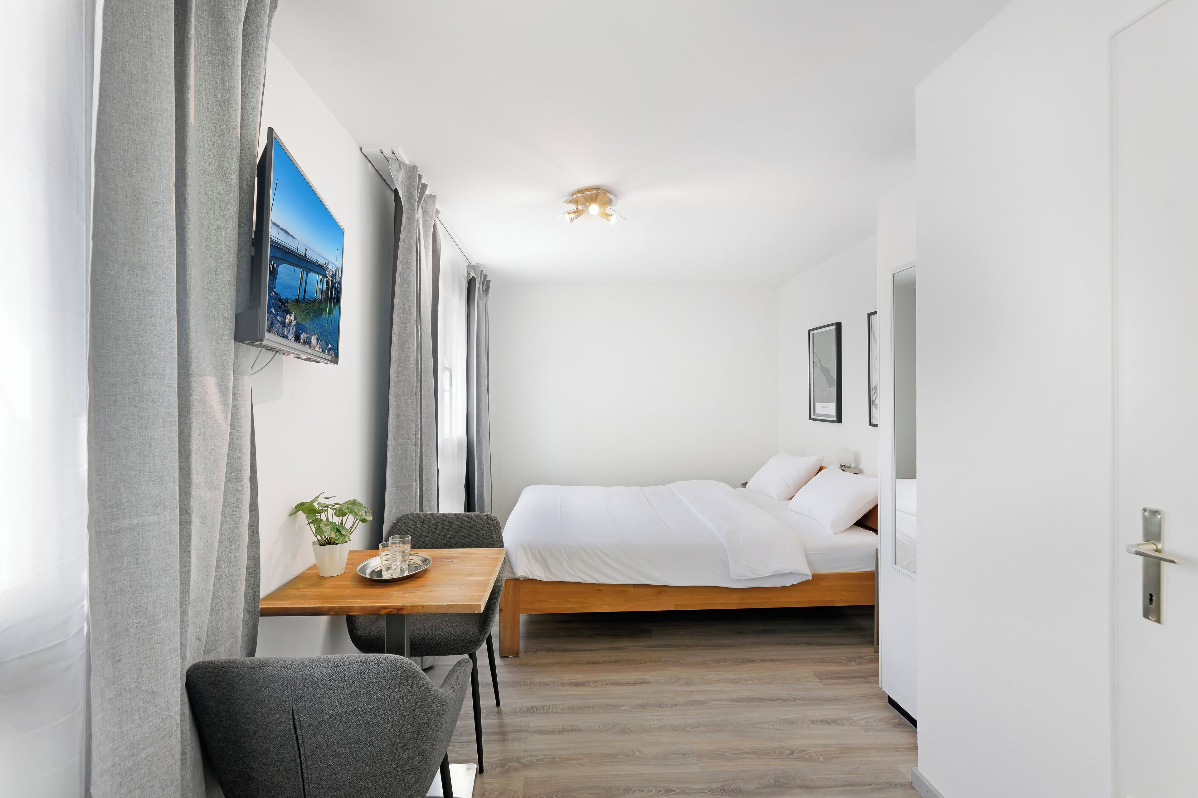 Hotelkamer met een bed, een bureau, een stoel, een kamerplant en een aan de muur bevestigde televisie.