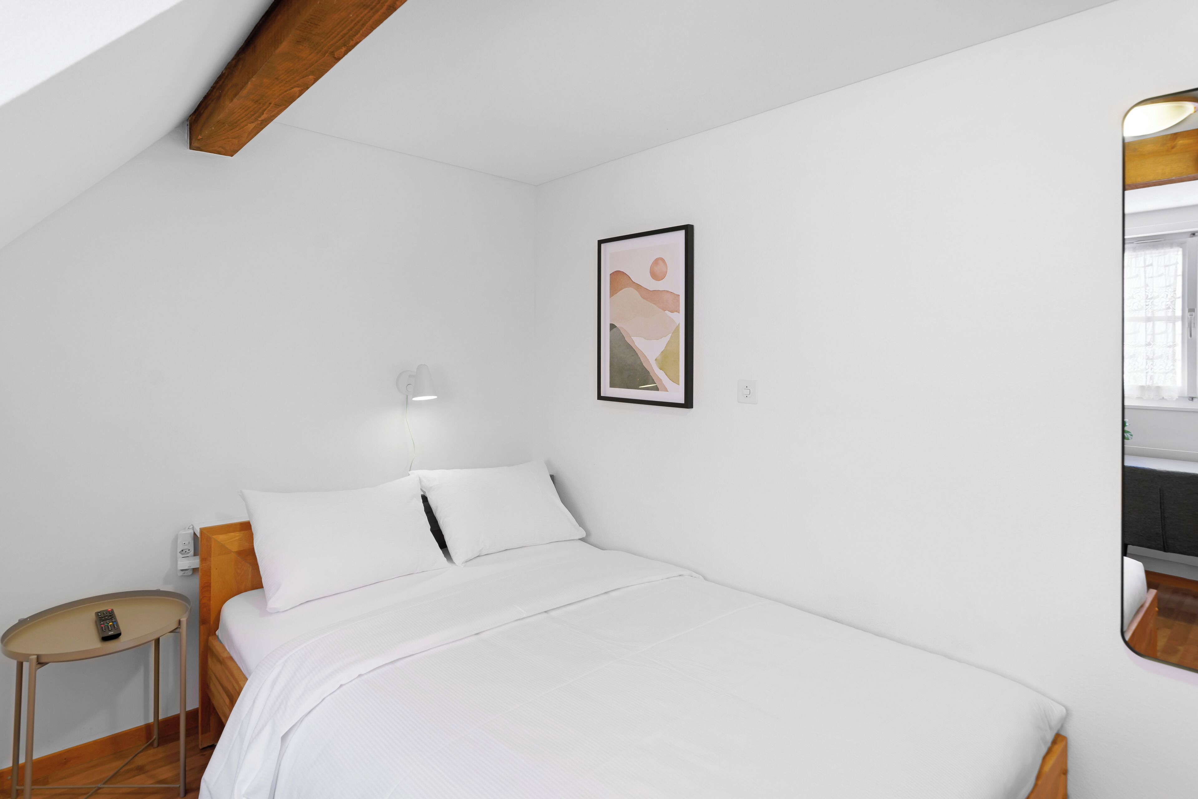 Un dormitorio con cama, mesita de noche, luz de pared y un cuadro enmarcado.