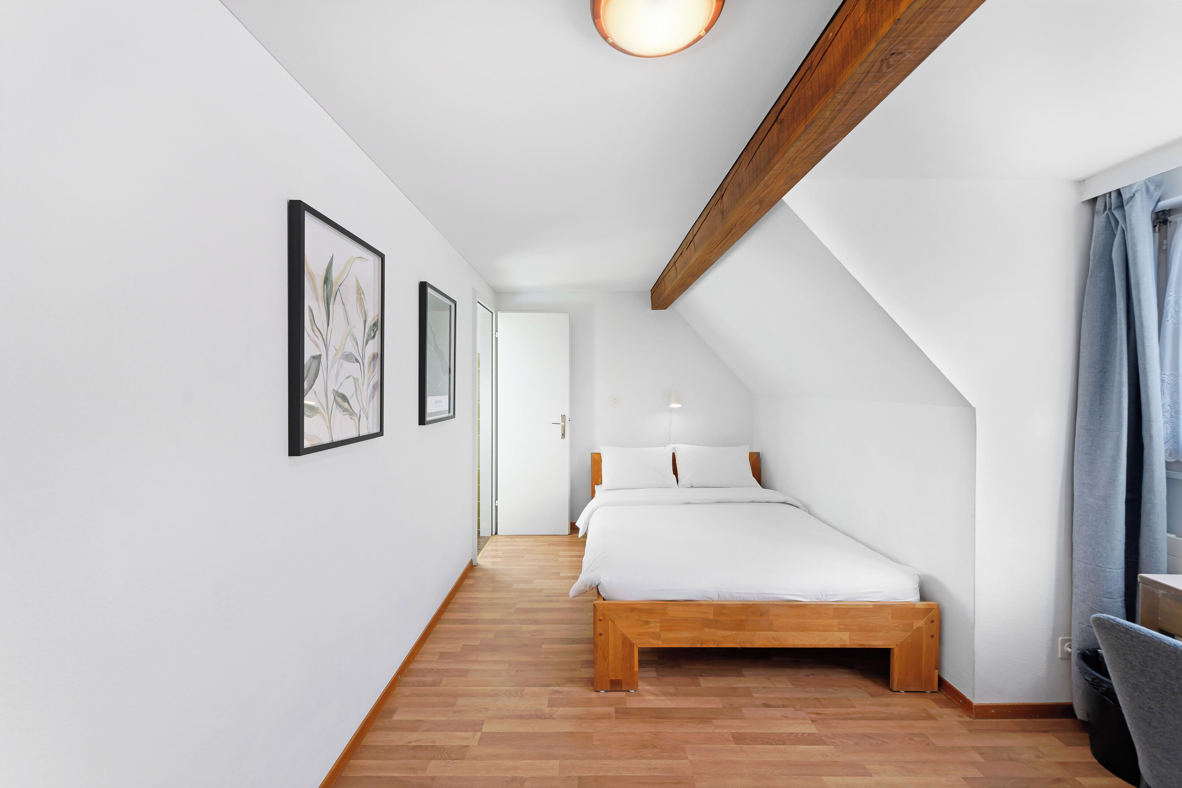 Un dormitorio con cama de madera, paredes blancas y una viga de madera en el techo.