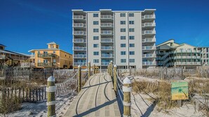 A beachside boardwalk leading to a multi-story building with balconies, surrounded by sand and vegetation. - Shoreline Towers (Gulf Shores)