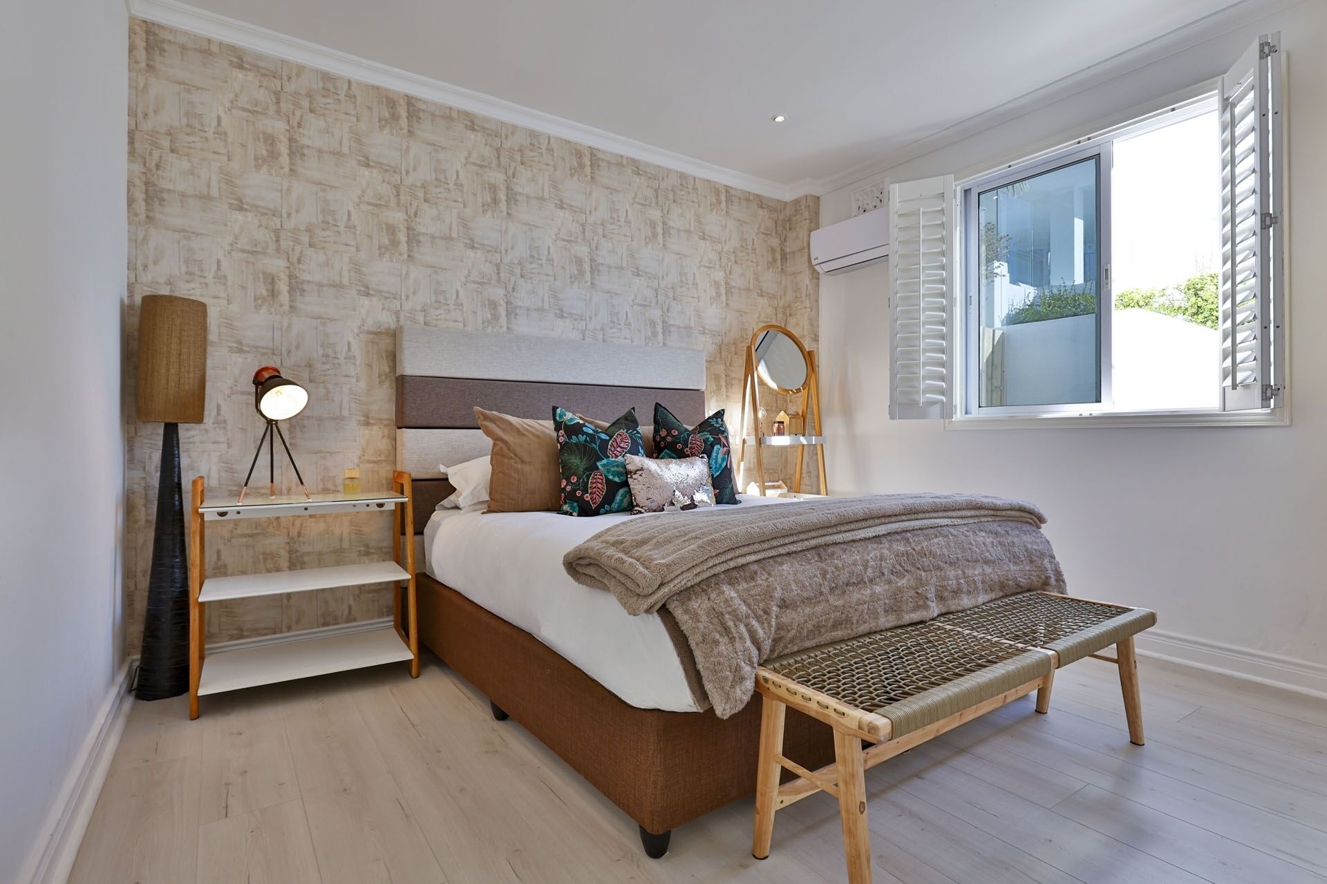 A bedroom with a bed, bedside tables, a lamp, a bench, and a window with shutters.