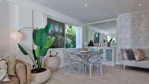 A modern living room with a dining table, clear chairs, a sofa, and a large potted plant. - YOLO Spaces - Clifton Boutique Villa (Cape Town)
