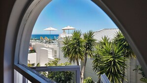 A balcony with a view of the sea, white buildings, and palm trees. - YOLO Spaces - Clifton Boutique Villa (Cape Town)