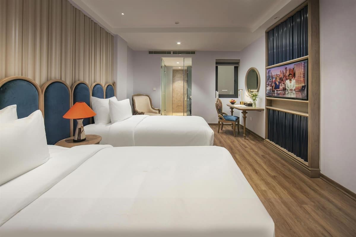 A hotel room with two beds, a desk, a chair, a mirror, and a television.