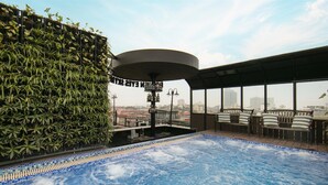 Une piscine sur le toit offrant une vue sur les gratte-ciel de la ville, entourée de verdure et agrémentée d’espaces aménagés avec des sièges confortables.