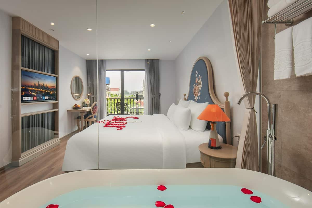 A hotel room with a bed, a TV, a bathroom with a bathtub, and a balcony with a city view.