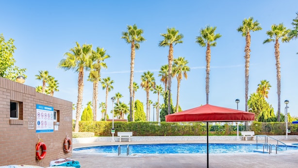 A swimming pool with palm trees, a lifebuoy, and a red umbrella. - Seafront Apartment 'Vistamar' with Sea Views, Wi-Fi & Air Conditioning (Oropesa)