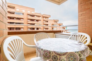Un balcón con una mesa y sillas, con vistas a un edificio de múltiples balcones y al mar.