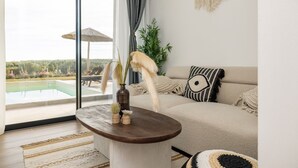 Una sala de estar con un ventanal grande, una mesa redonda de madera y un sofá beige con cojines estampados.