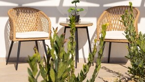 Un patio soleado con dos sillas de mimbre, una mesita y una planta en maceta.