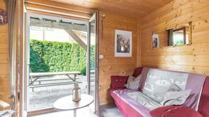 L’intérieur d’un chalet en bois, avec un canapé, une table et une vue sur une haie verdoyante à l’extérieur.