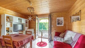 Un intérieur de chalet chaleureux avec un coin repas, un canapé, un téléviseur et une grande fenêtre.