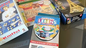 Une variété de jeux de société, notamment le Scrabble, le Monopoly et d’autres, sont disposés sur une table en verre.