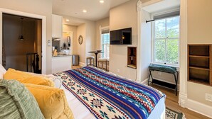 A bedroom with a bed, a ceiling fan, a TV, and a window with a view of trees. - The Claret Cup Suite at The Hesch - Premier Location- Railyard Arts District (Santa Fe)