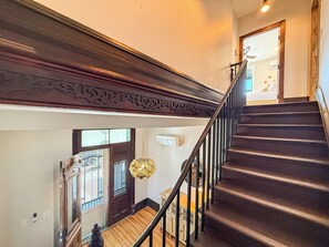 Una escalera con escalones oscuros y barandal de madera, que conduce a un rellano con una puerta y una ventana.