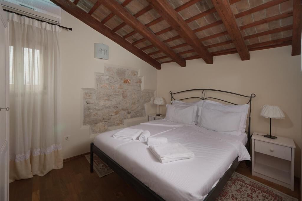 Una camera da letto con parete in pietra, un letto con lenzuola bianche, due comodini con lampade e soffitto in legno.
