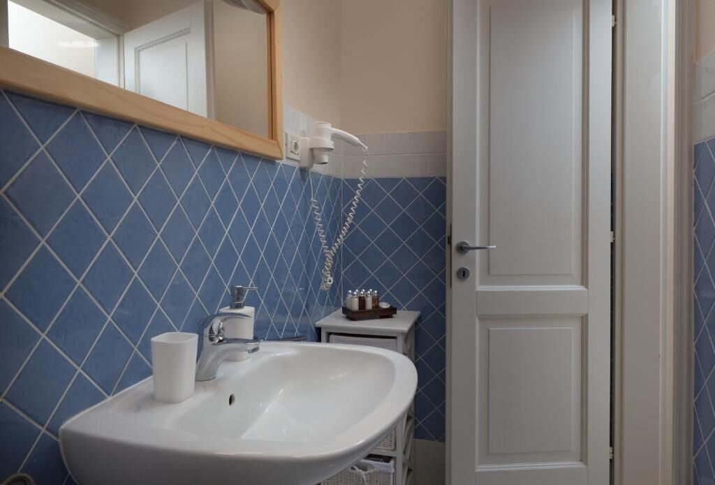 A bathroom with a white sink, blue diamond-patterned tiles, a white door, and a small cabinet with toiletries.
