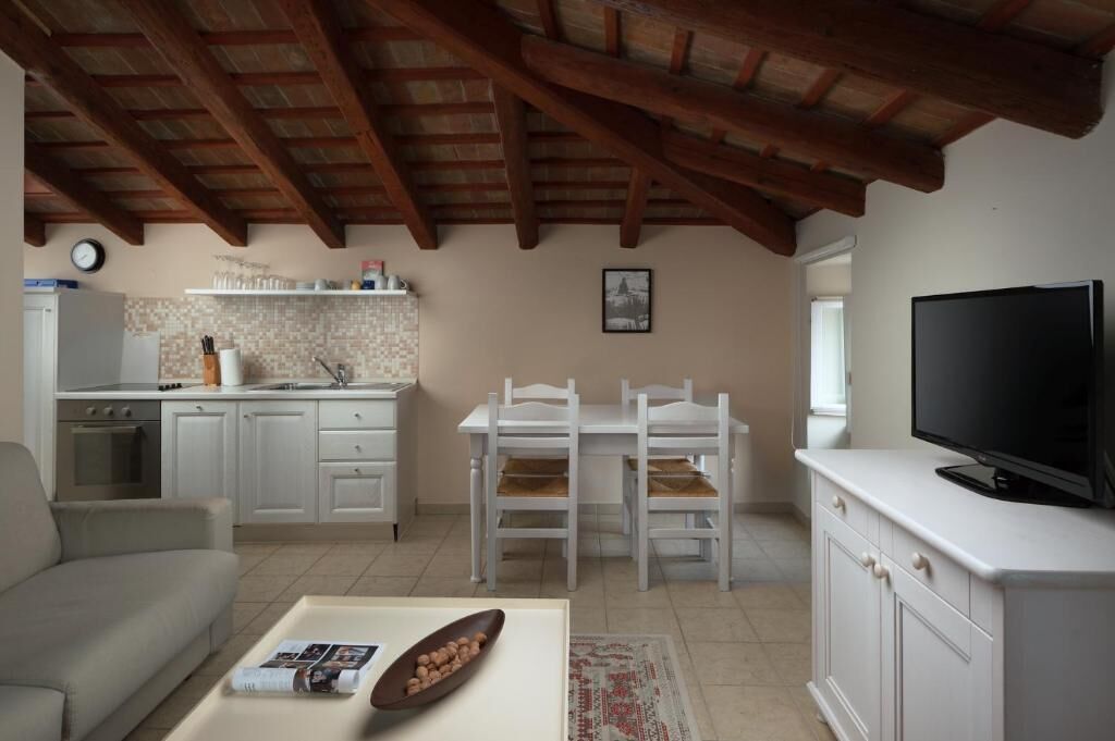 Eine moderne Küche mit weißen Schränken, einem Esstisch mit Stühlen, einer Couch, einem Fernseher und einer Uhr an der Wand.