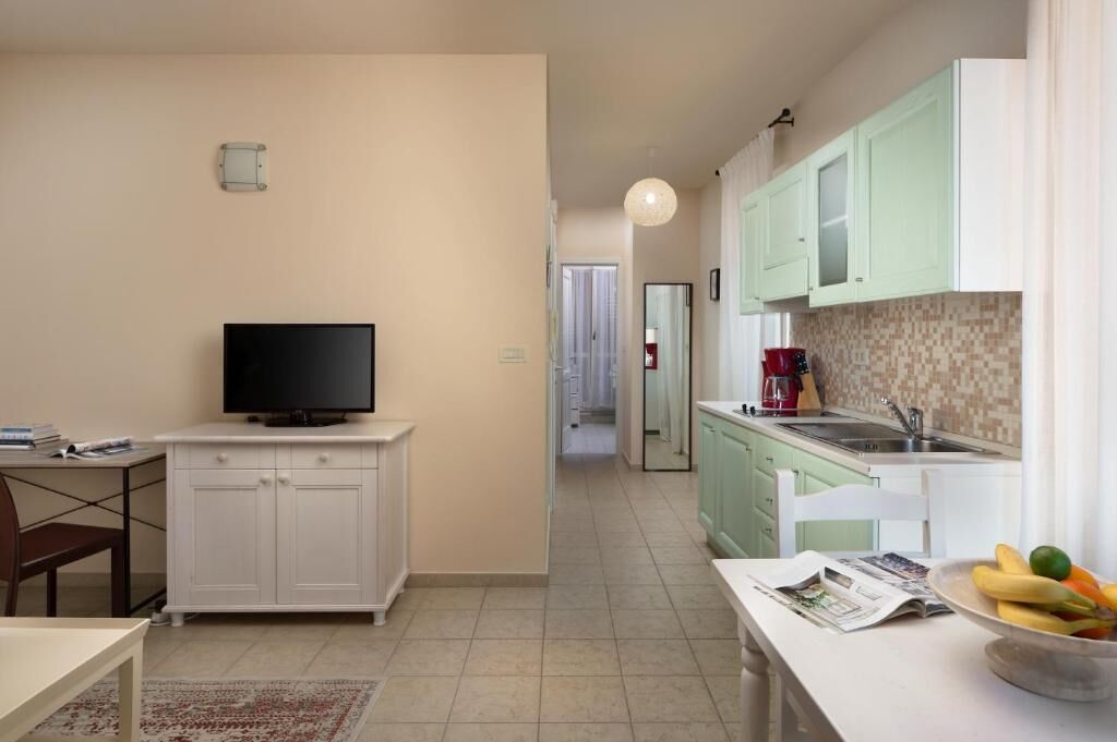 A compact kitchen with a TV, a dining area, and a small table with a bowl of fruit.