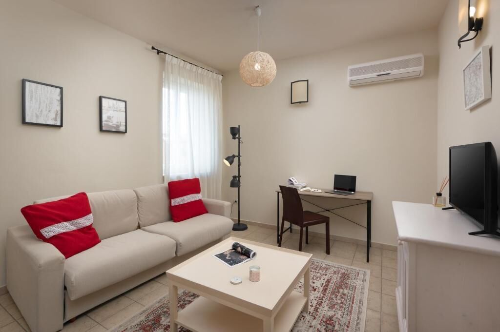 Un soggiorno moderno con un divano color beige, un tavolino, una scrivania con un portatile, una TV e una lampada a sospensione.