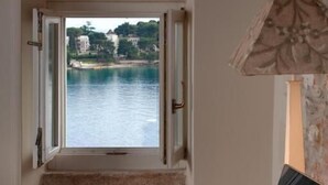 Ein Zimmer mit Blick auf ein Gewässer durch ein offenes Fenster, ein Laptop auf einem Tisch und ein Stuhl.