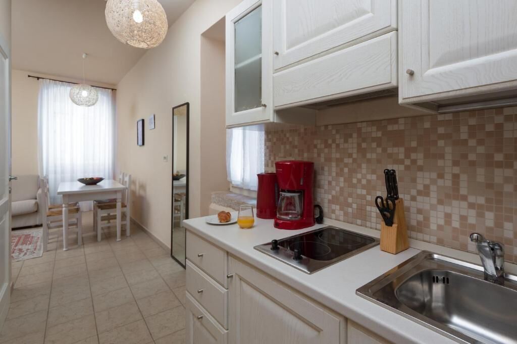 Cocina compacta con muebles blancos, cafetera y lavabo.